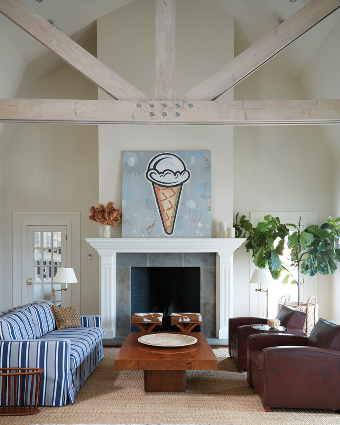 The guest house living room includes a loveseat covered in a Ralph Lauren stripe fabric, a pair of 1930s French leather armchairs, and playful art by Donald Baechler. The vintage teak slab table is from Jalan Jalan in Miami.